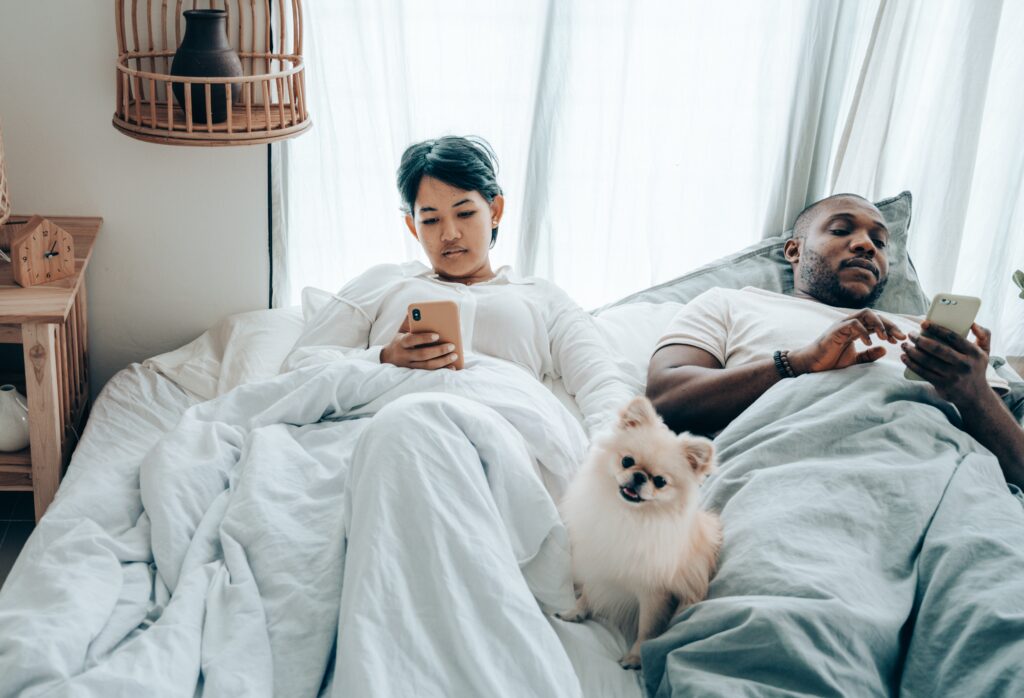 Una coppia di persone è a letto ma non si parlano perchè stanno usando il telefono.